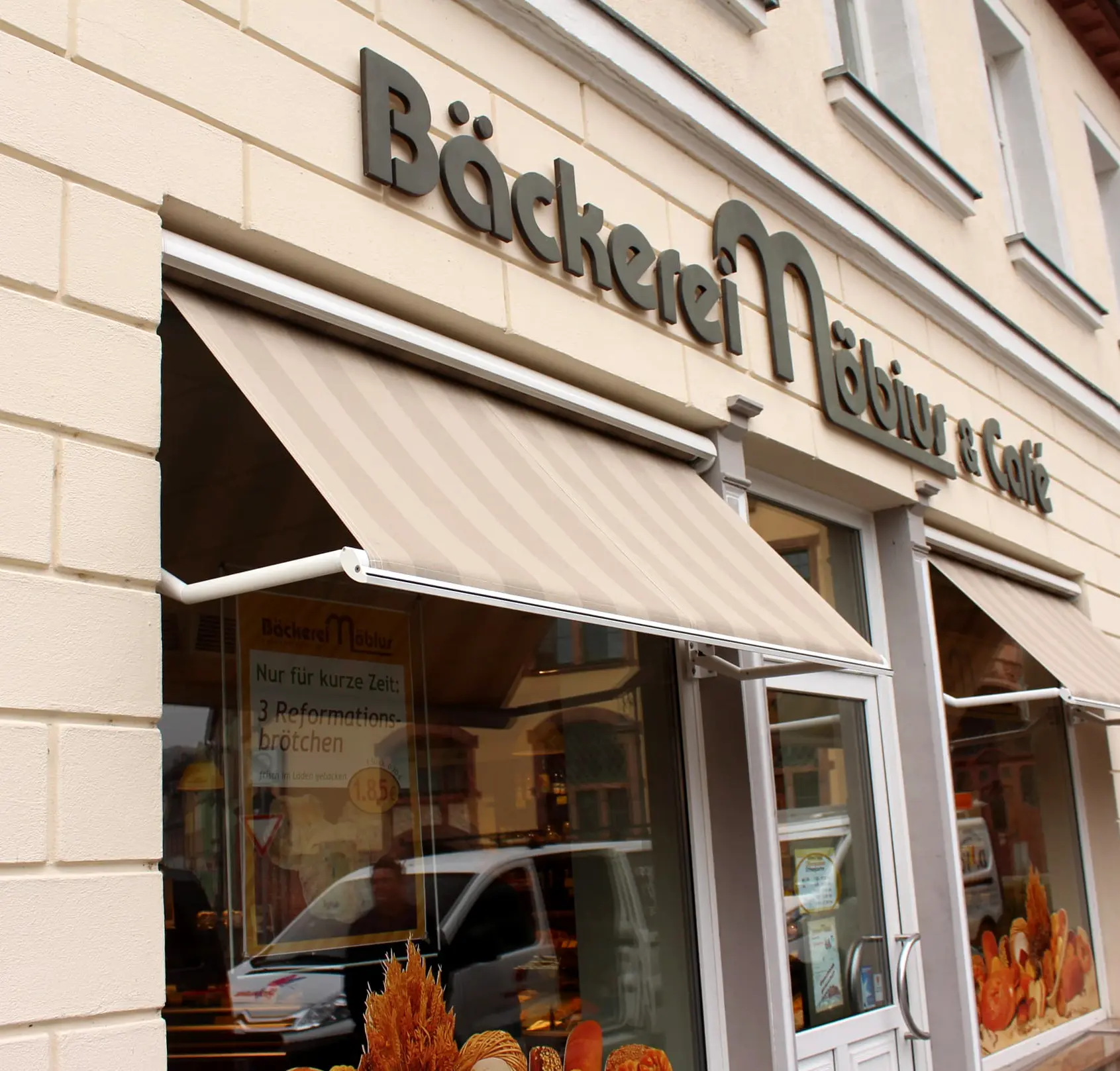 Fenstermarkise an einer Bäckerei in harmonischen Beigetönen für stilvollen Sonnenschutz