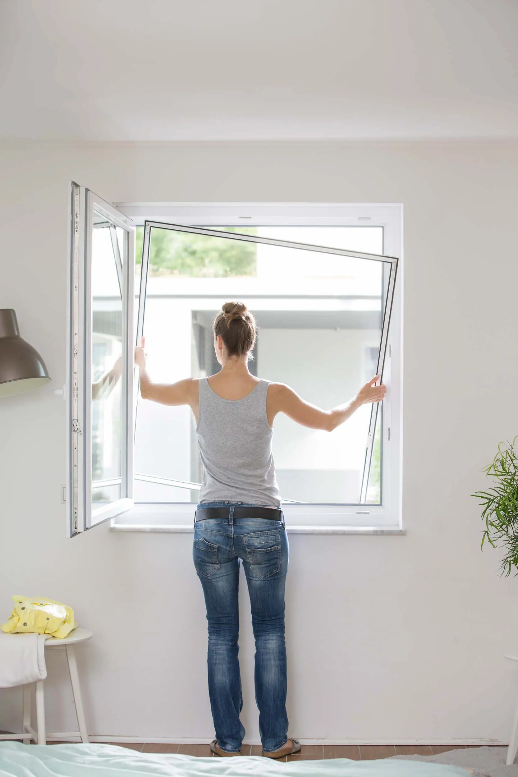 Frau hängt Insektenschutzfenster mit TTA Premium-Gewebe ein, fast unsichtbar, luftdurchlässig und sicher vor Insekten, hochwertige Aluminiumprofile, maßgefertigt